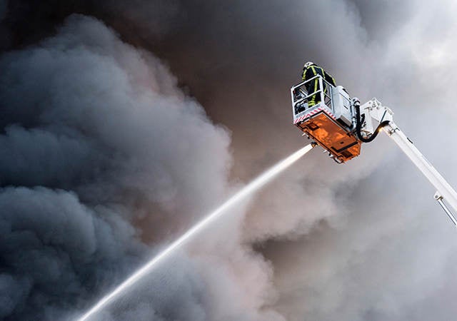 Firefighter on aerial ladder spraying hose against smoky sky